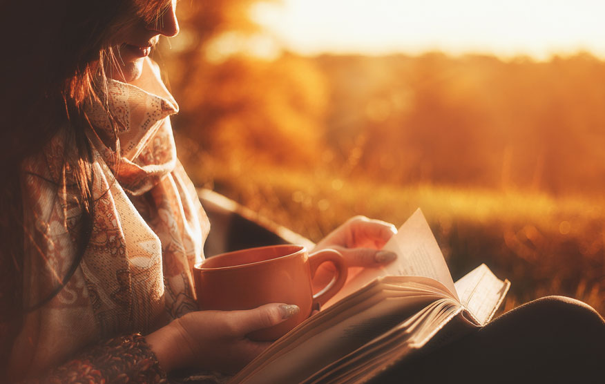 Eine entspannte Frau trinkt Tee und liest ein Buch, während sie ihre Frauenpower mit einer Auszeit stärkt.